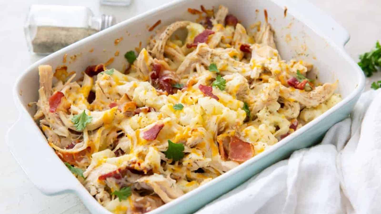 Keto Chicken Bacon Ranch with cauliflower, cheese, and parsley in a white casserole dish with a wooden spoon.