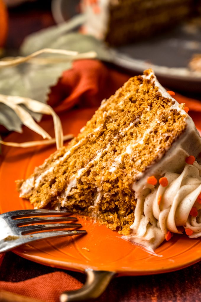 A slice of pumpkin cake on a plate with a fork and a bite has been taken from the cake.